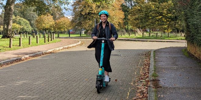 A young woman riding a TIER branded e-scooter with green space in the background